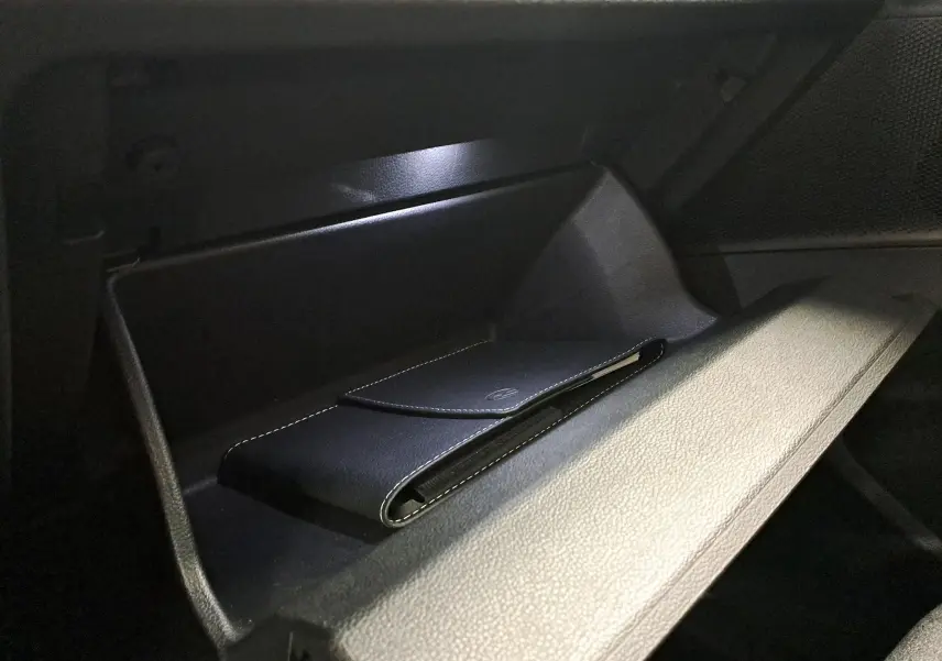 Gros plan sur la boîte à gants ouverte du Volkswagen Tiguan 2024, avec un étui noir à l'intérieur, éclairage intérieur visible.
