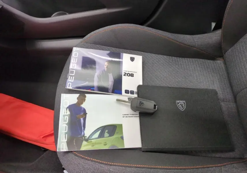 Vue intérieure du siège avant droit gris clair d'une Peugeot 208 avec clés et manuels posés dessus.