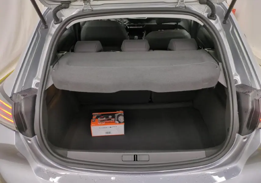 Coffre ouvert d’une Peugeot 208 gris clair, vue arrière montrant un kit de dépannage pneumatique posé au sol.