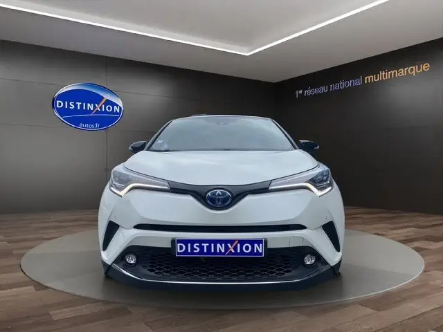 Vue frontale d'un Toyota C-HR Hybride blanc avec toit noir, éclairage LED distinctif et plaque Distinxion visible.