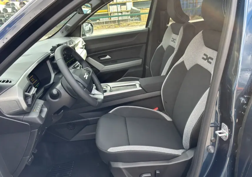Intérieur avant droit du Dacia Bigster Hybrid 155 Journey Plus bleu indigo, sièges bi-ton gris et noir avec volant cuir.