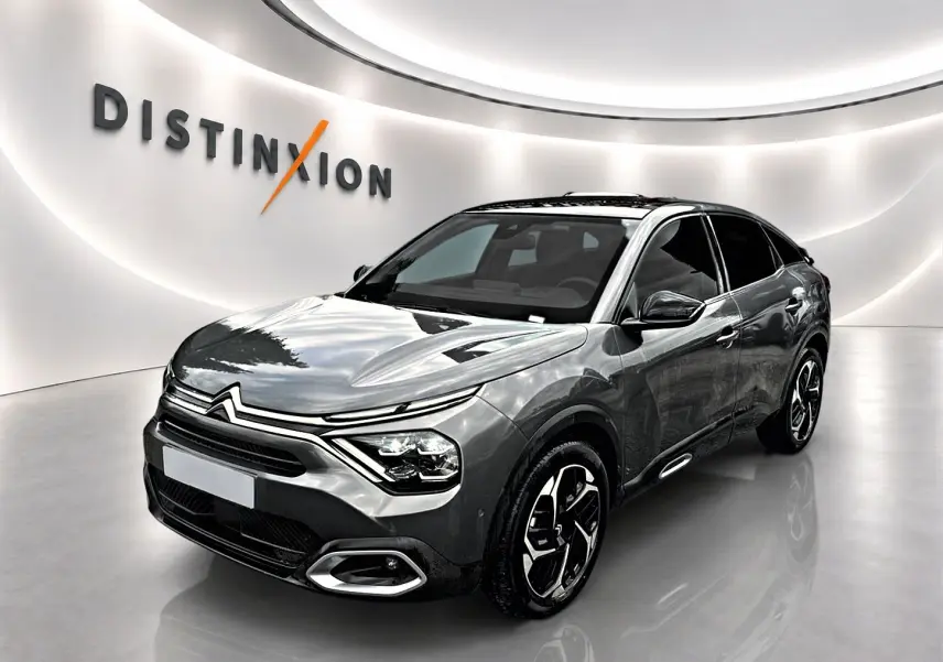 Citroën C4 gris 3/4 avant droit, avec jantes noires et toit panoramique en showroom lumineux.