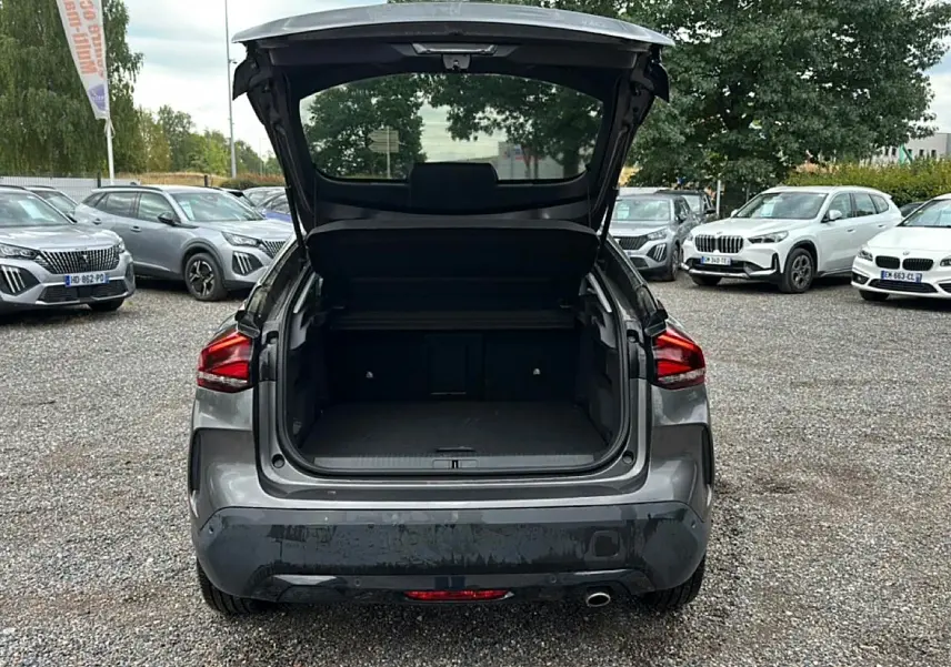 Vue arrière d'une Citroën C4 gris 2024 avec coffre ouvert sur un parking extérieur.