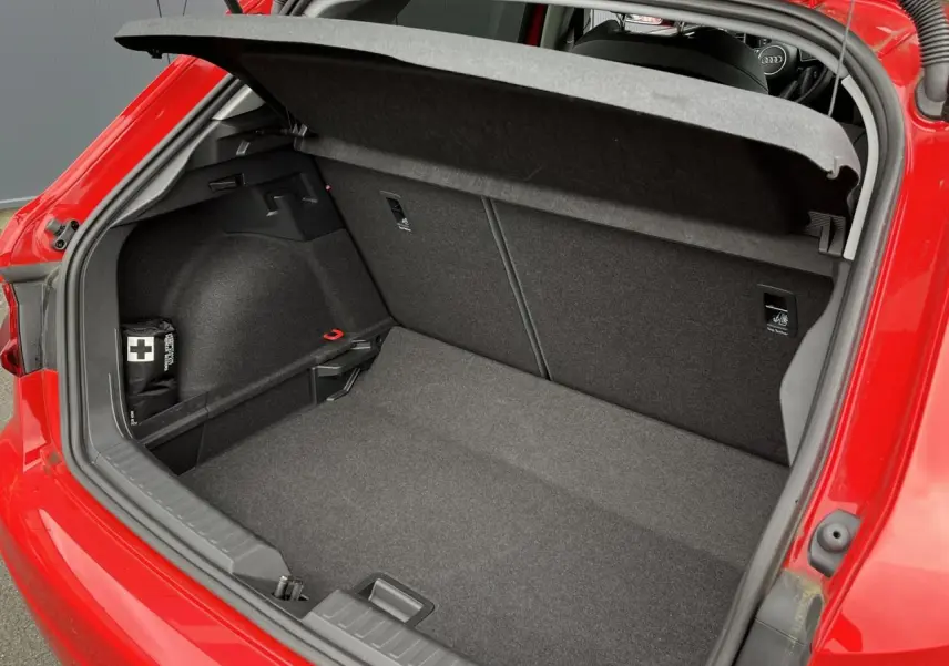 Coffre ouvert vu de l'arrière d'une Audi A1 Sportback rouge Misano avec intérieur de coffre gris et trousse de secours.