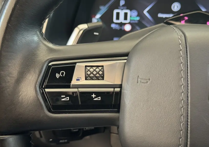 Gros plan sur les commandes gauche du volant cuir noir du DS7 Crossback E-TENSE 4x4, avec tableau de bord numérique en arrière-plan.