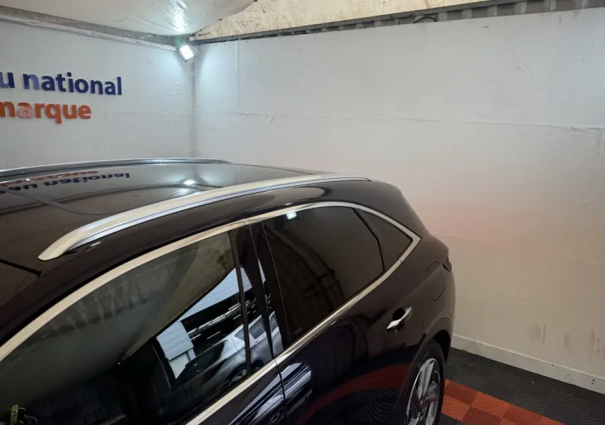 Vue latérale droite du DS7 Crossback bleu avec barres de toit chromées et vitres teintées dans un garage.