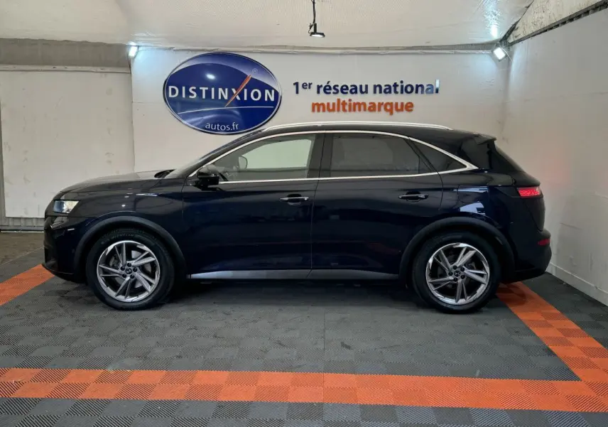 Vue latérale droite d'un DS7 Crossback E-TENSE bleu avec toit noir, dans un showroom au sol gris et orange.