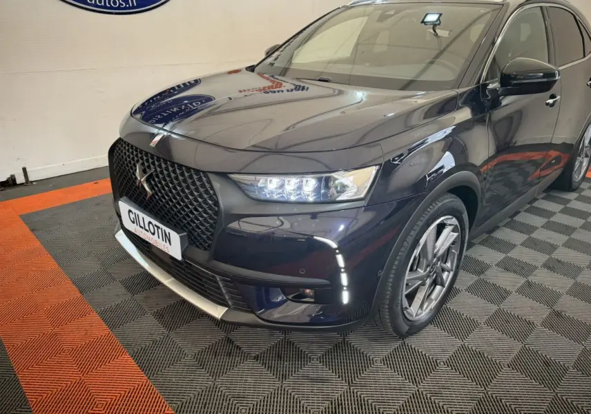 Vue 3/4 avant droit du DS7 Crossback E-TENSE bleu avec calandre noire et feux LED allumés en intérieur showroom.