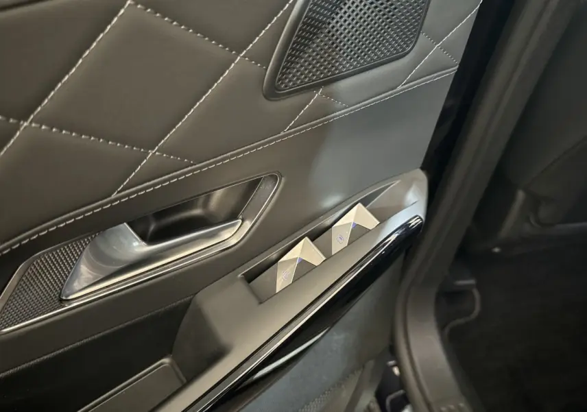 Gros plan sur la porte intérieure côté gauche du DS7 Crossback bleu, avec commandes de vitres et surpiqûres apparentes.