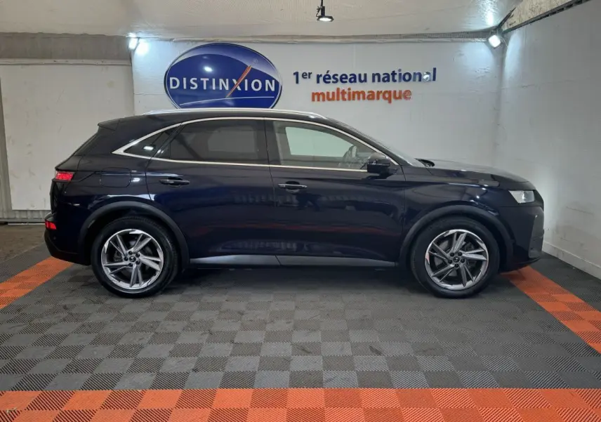 Vue latérale droite d'un DS7 Crossback E-TENSE bleu foncé dans un showroom avec sol gris et orange.