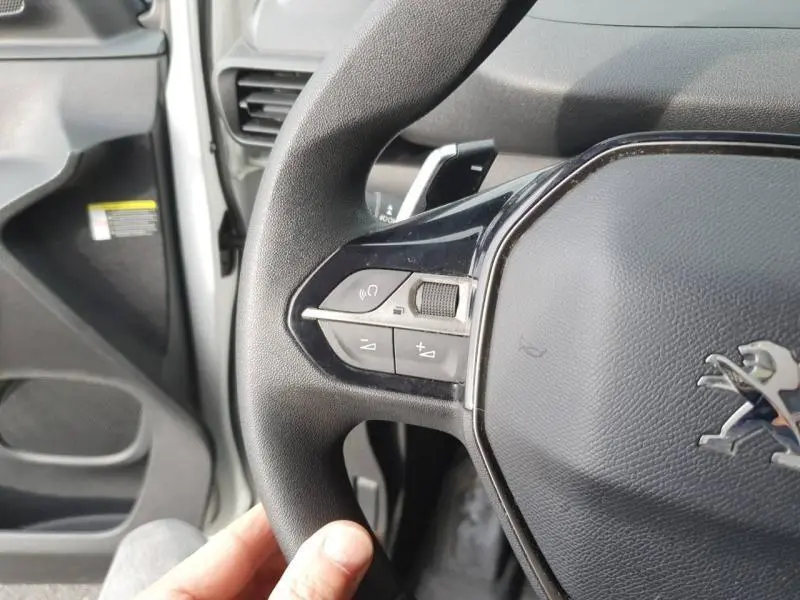 Gros plan sur le volant noir du Peugeot Partner blanc, montrant les commandes audio sur le côté gauche.