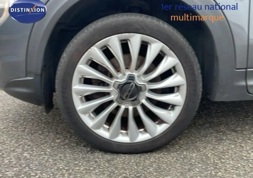 Gros plan sur la jante alliage 18 pouces argentée du côté avant droit d'une FIAT 500X gris foncé.