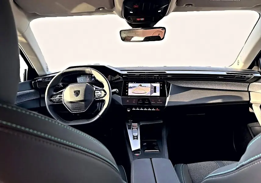 Vue intérieure avant du Peugeot 408 Hybrid noir 2025, avec tableau de bord moderne et écran tactile affichant la caméra de recul.