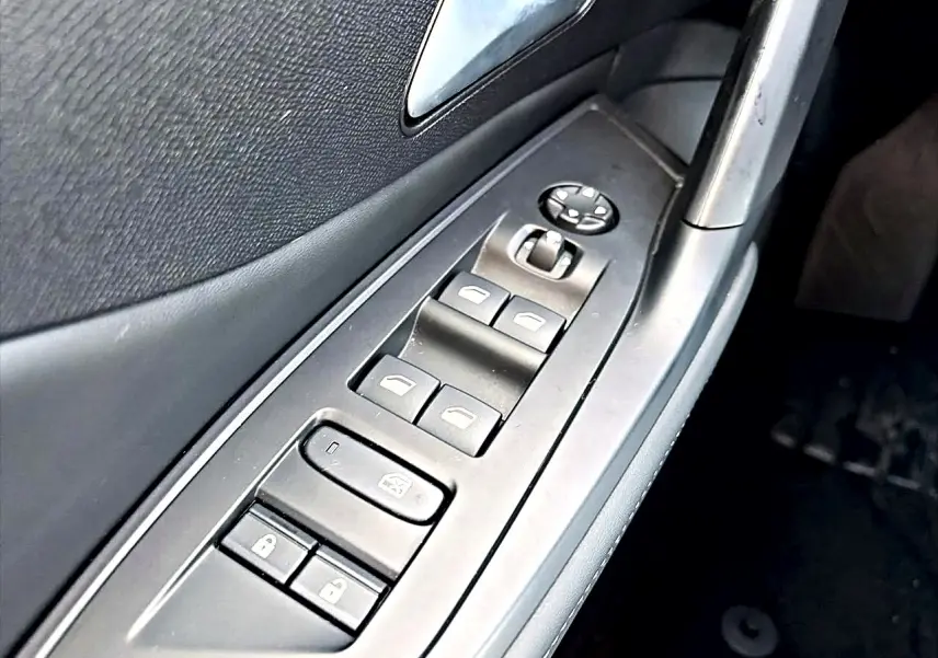 Gros plan sur les commandes des vitres et rétroviseurs côté conducteur d'une Peugeot 408 noire, intérieur sombre.
