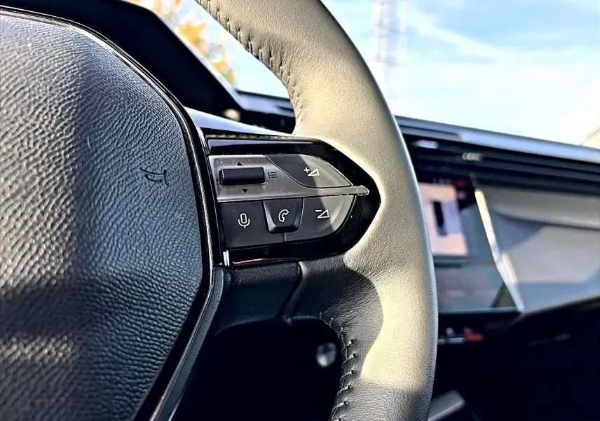 Gros plan sur le volant cuir noir de la Peugeot 408 Hybrid 145 allure e-dcs6 avec commandes vocales et multimédia visibles.