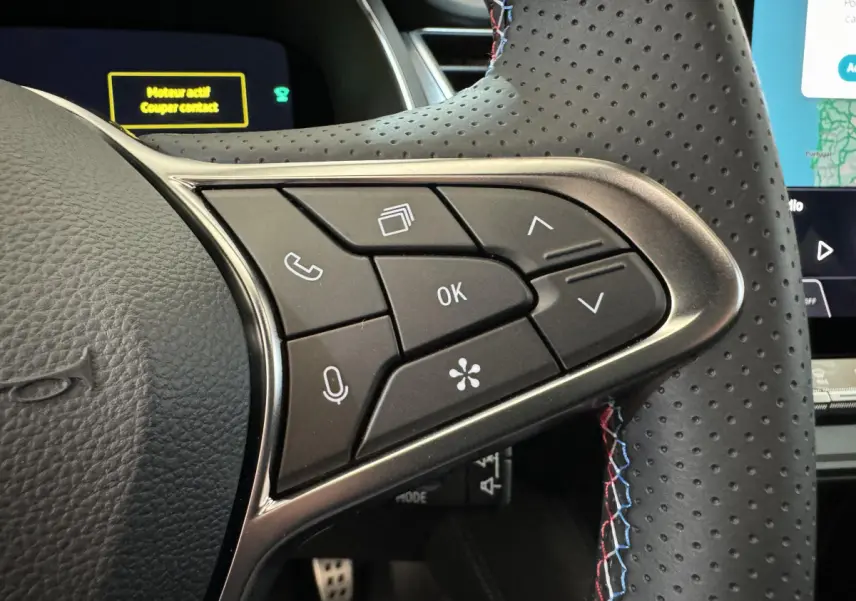 Gros plan sur les commandes multifonctions à droite du volant perforé avec surpiqûres tricolores dans un Renault Captur blanc esprit Alpine E-Tech 2025.