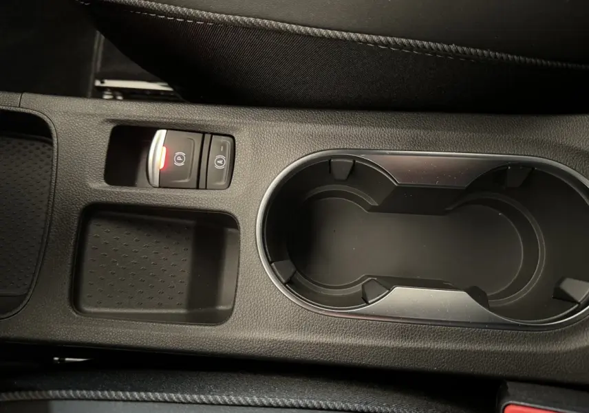 Gros plan sur la console centrale noire du Renault Captur blanc, avec porte-gobelets et bouton de frein à main électrique allumé.