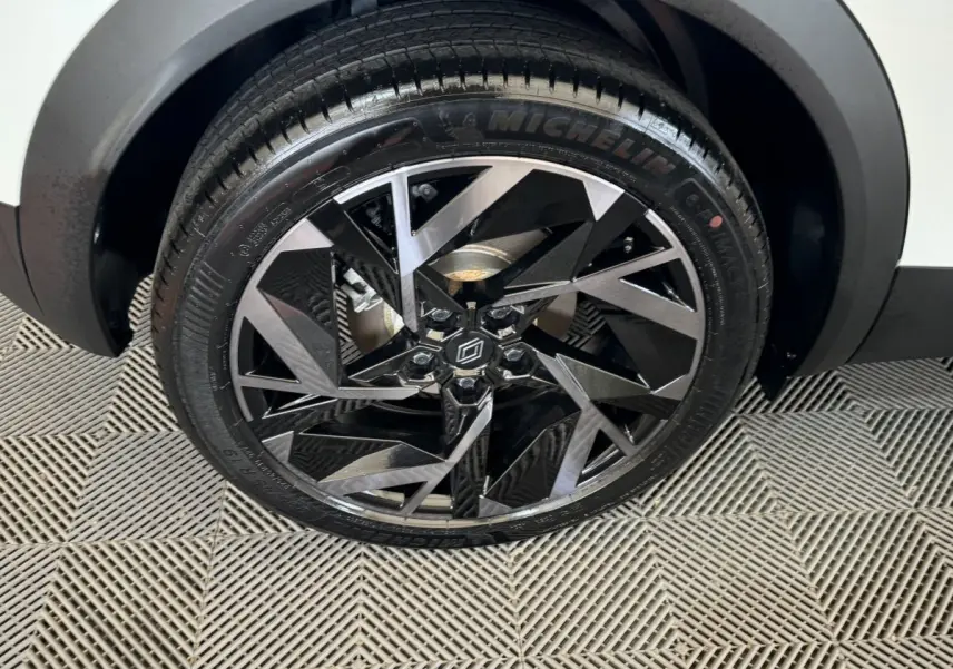 Gros plan sur la roue avant droite du Renault Captur blanc, jante alliage noire et argent au design géométrique.