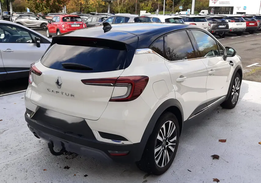 Vue 3/4 arrière droite d'un Renault Captur blanc au toit noir, avec jantes alliage et vitres teintées, stationné en extérieur.