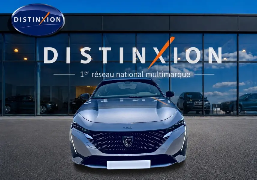 Vue de face d'une Peugeot 308 gris métallisé avec calandre noire et logo lion, devant une vitrine Distinxion.