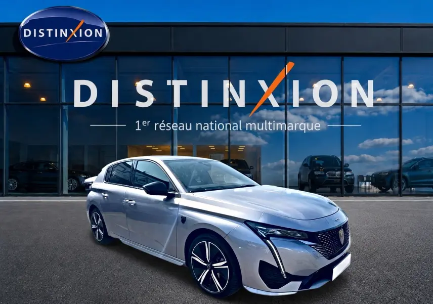 Peugeot 308 gris vue 3/4 avant droit, avec calandre distinctive et jantes alliage modernes devant showroom Distinxion.