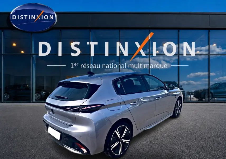 Peugeot 308 gris en vue 3/4 arrière droit, avec jantes alliage et feux arrière LED distinctifs, devant un showroom Distinxion.