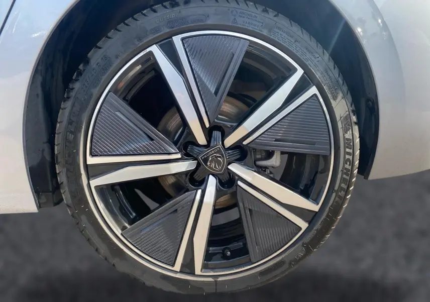 Gros plan sur la jante alu noire et argentée d’une Peugeot 308 gris clair, mettant en valeur le logo central Peugeot.