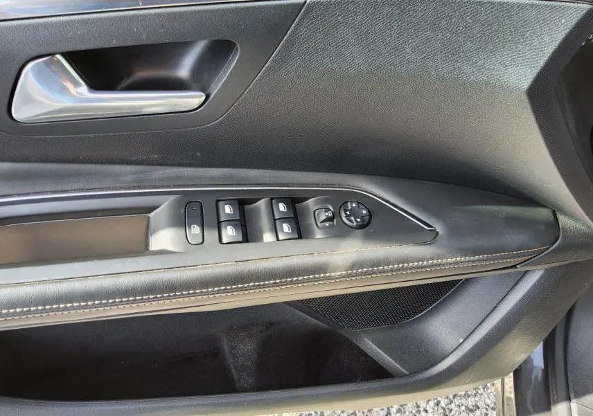 Gros plan sur la porte conducteur intérieure noire avec commandes des vitres et poignée chromée du Peugeot 3008 gris métallisé.