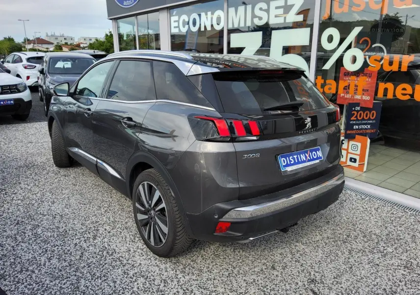 Vue 3/4 arrière droite d'un Peugeot 3008 gris métallisé avec jantes alliage et toit noir devant une vitrine commerciale.