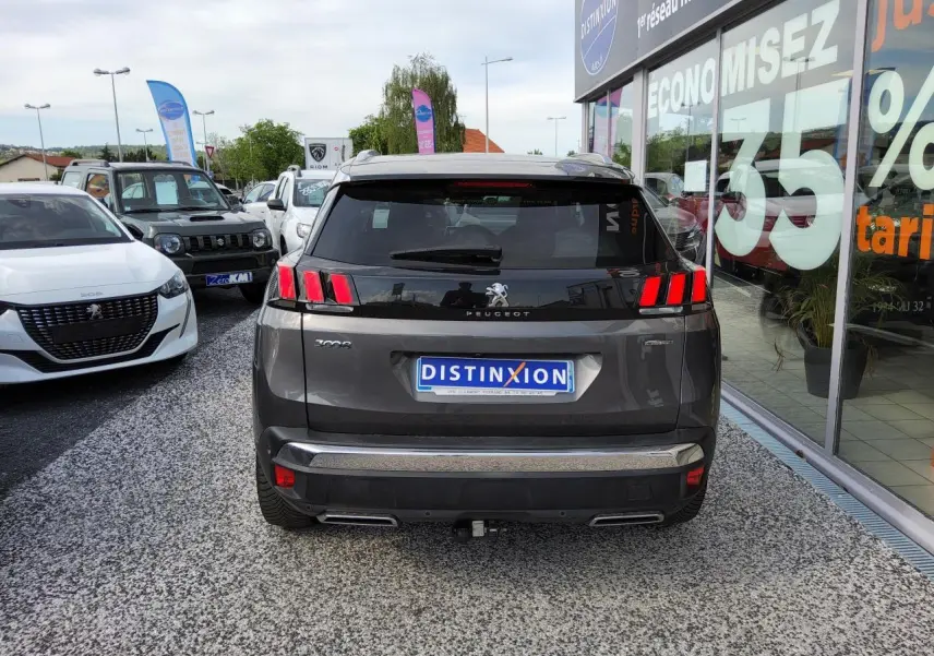 Vue arrière d'un Peugeot 3008 gris métallisé avec barres de toit et attelage visible sur parking de concession.