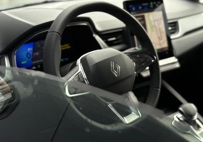 Vue intérieure rapprochée du volant en cuir et de l'écran tactile vertical du tableau de bord du Renault Symbioz gris Rafale.
