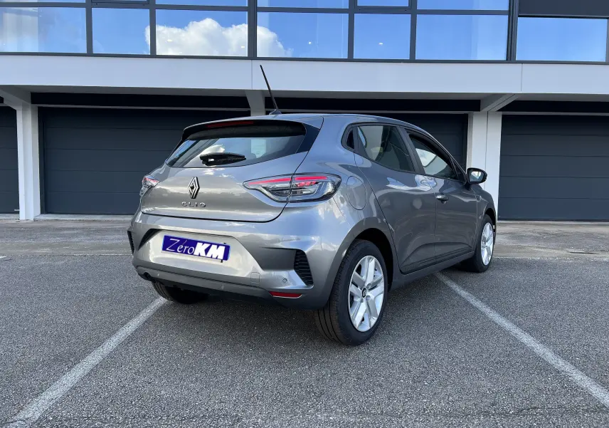 Renault Clio V gris schiste vue 3/4 arrière droit, jantes alliage 16 pouces et protections latérales chromées visibles.