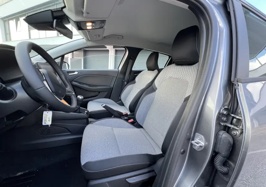 Intérieur avant droit de la Renault Clio V gris schiste 2025, sièges tissu bicolore et volant multifonctions.