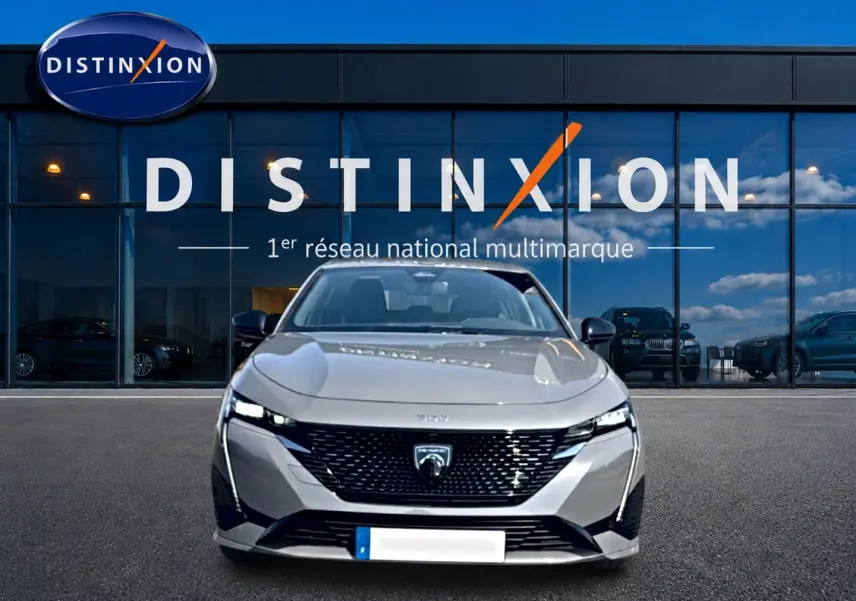 Vue de face d'une Peugeot 308 gris métallisé garée devant une vitrine avec logo Distinxion.