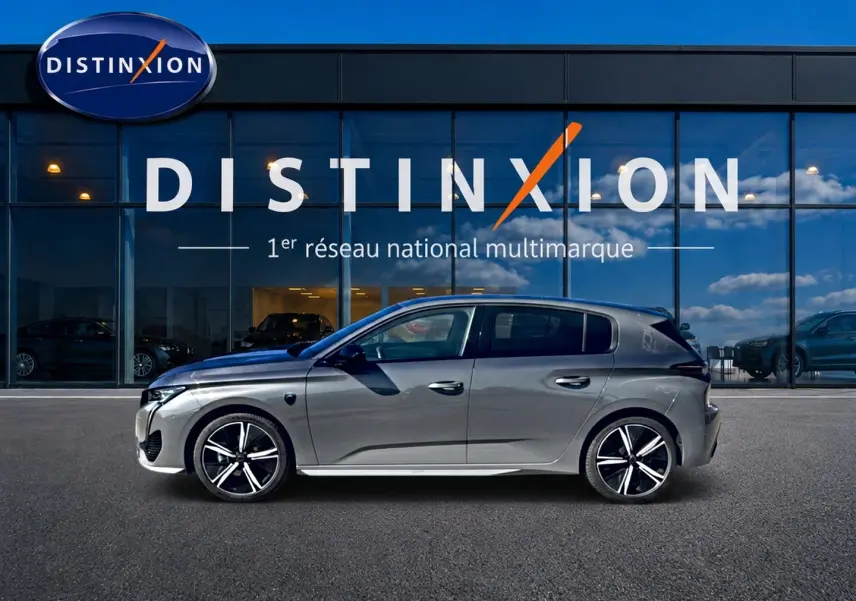 Profil droit d'une Peugeot 308 gris métallisé 2025 garée devant une vitrine avec logo Distinxion.