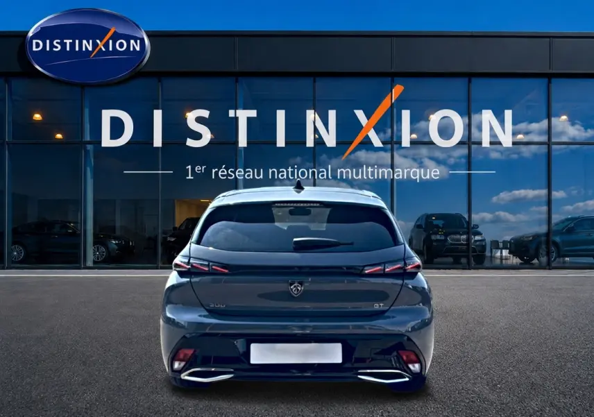 Vue arrière d'une Peugeot 308 gris métallisé garée devant une vitrine avec logo Distinxion.