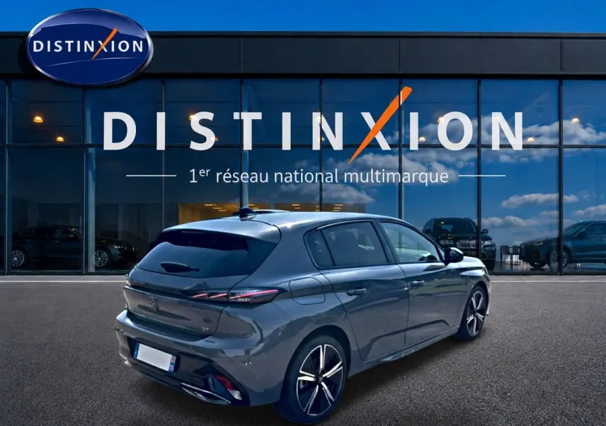 Vue 3/4 arrière droite d'une Peugeot 308 gris métallisé avec jantes alliage, stationnée devant un showroom Distinxion.