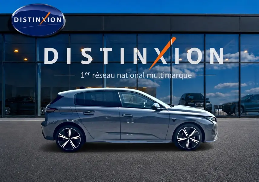 Profil droit d'une Peugeot 308 gris métallisé 2025 garée devant une vitrine avec logo Distinxion.