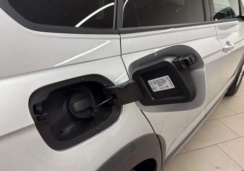 Vue latérale droite du Volkswagen Taigo gris cendré 2024 avec trappe à carburant essence ouverte sur un sol carrelé.
