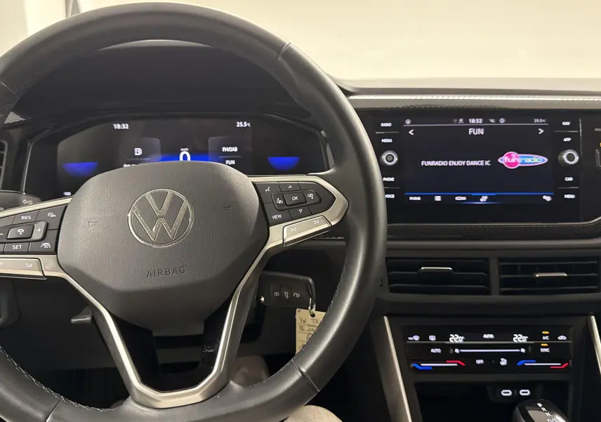 Vue intérieure du tableau de bord du Volkswagen Taigo 2024 avec volant multifonction et écran tactile central allumé.