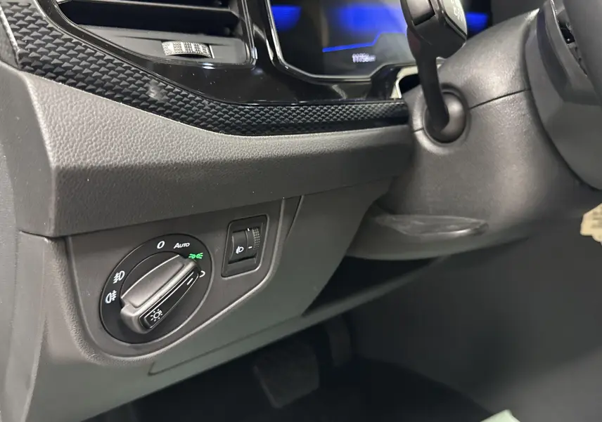 Gros plan sur le tableau de bord côté gauche du Volkswagen Taigo gris cendré, montrant la commande des phares et l'ambiance intérieure noire.