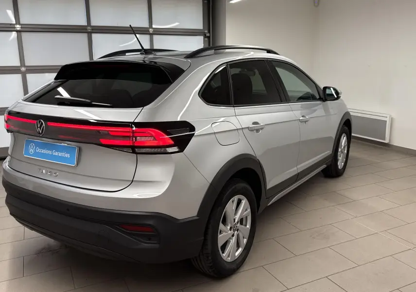 Volkswagen Taigo gris cendré vu de l'arrière côté droit, avec feux arrière allumés et toit noir brillant.