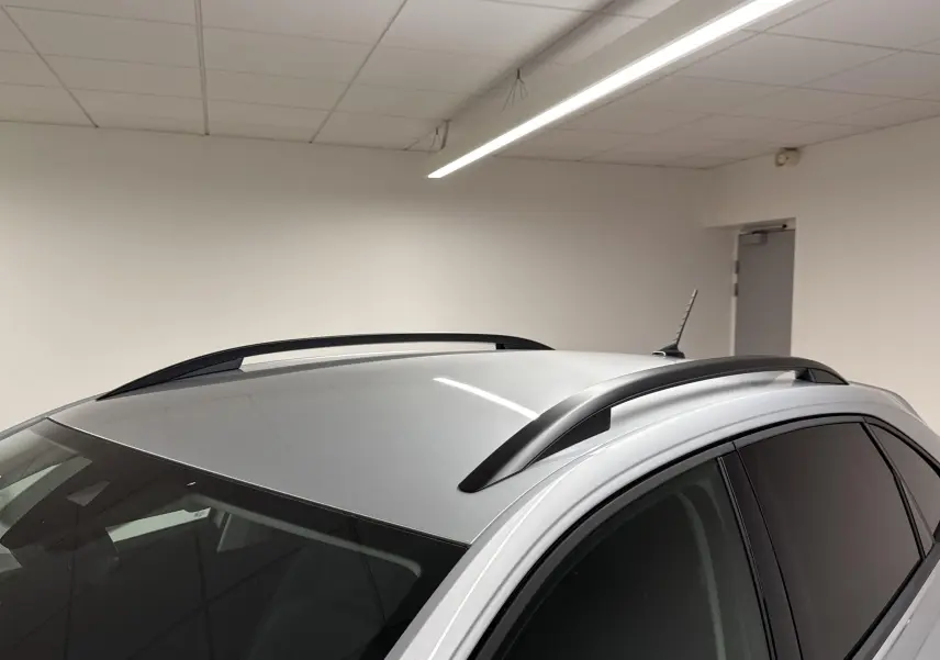 Vue 3/4 arrière du Volkswagen Taigo gris cendré 2024 avec barres de toit noires dans un garage blanc.