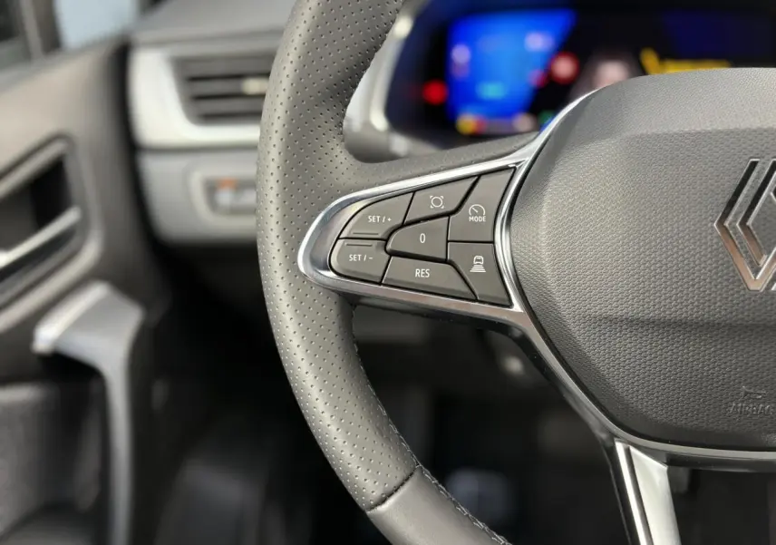 Gros plan sur le volant en cuir gris perforé de la Renault Symbioz 2025 avec commandes multifonctions et logo au centre.