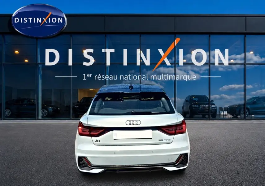 Vue arrière d'une Audi A1 Sportback 30 TFSI gris arrow avec feux LED et diffuseur noir, stationnée devant un showroom Distinxion.