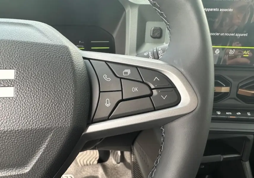Gros plan sur les commandes au volant à droite du Dacia Duster III gris schiste, avec écran tactile et tableau de bord partiel visible.