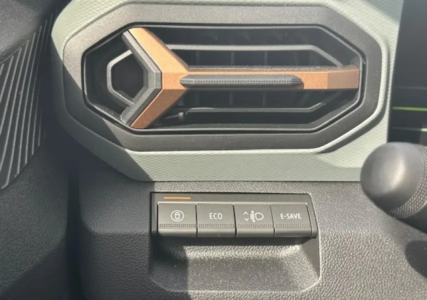 Gros plan sur la commande éco-mode et la sortie d'air hexagonale intérieure du Dacia Duster 2025 gris schiste.