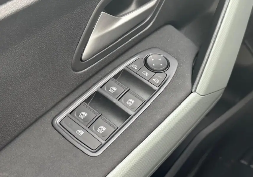 Gros plan sur les commandes des vitres électriques côté conducteur du Dacia Duster III gris schiste, intérieur moderne et épuré.