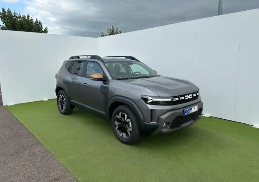 Dacia Duster III gris schiste métal vu en 3/4 avant droit avec barres de toit noires et jantes alliage.