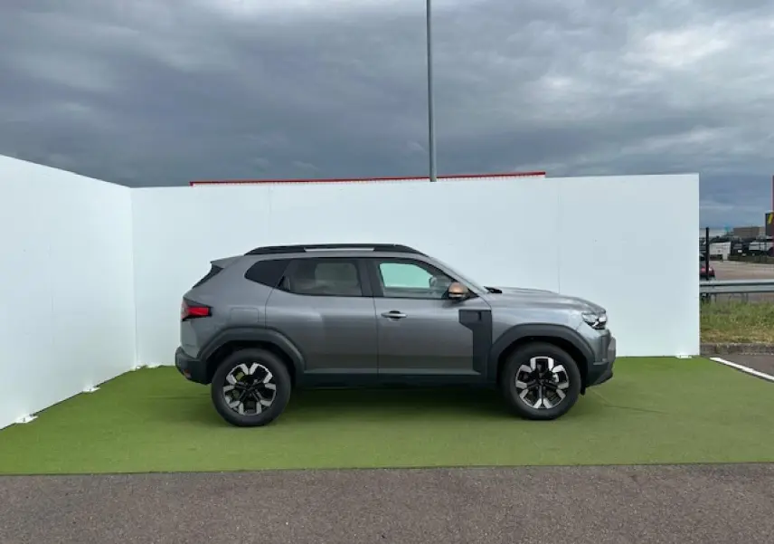 Profil côté gauche du Dacia Duster III gris schiste métal avec jantes alliage et barres de toit noires sur fond extérieur.